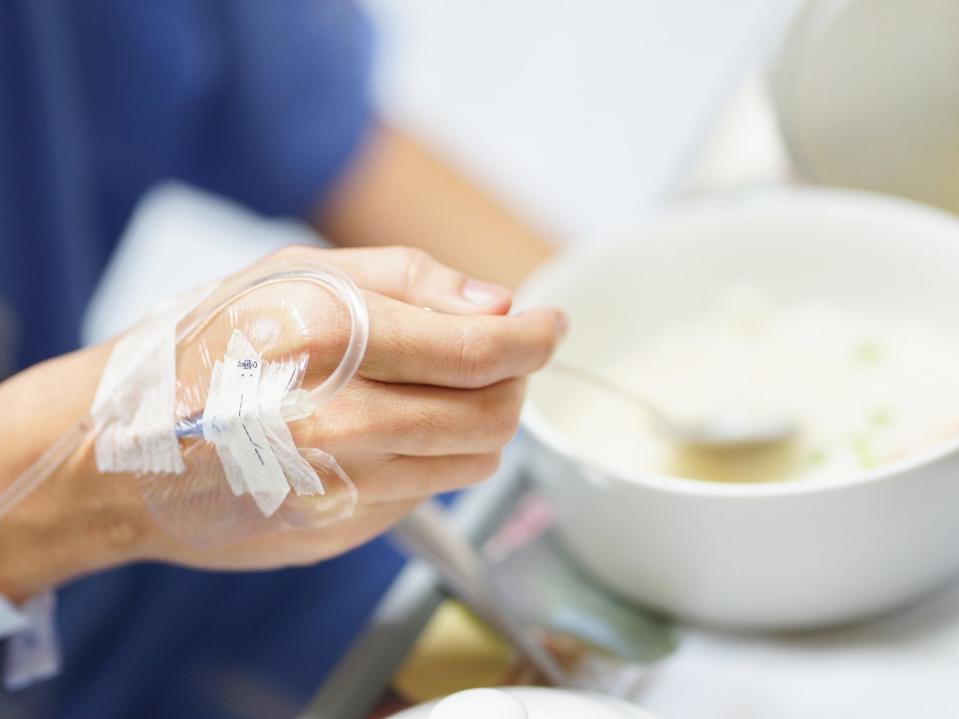 Dettaglio di una mano con flebo durante un pasto, a rappresentare l’importanza di una corretta scelta alimentare nei trattamenti oncologici.