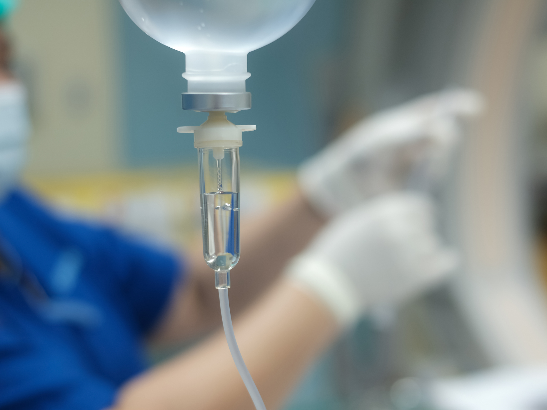 Dettaglio di una flebo con operatore sanitario sullo sfondo, a illustrazione del tema alimentazione e gestione degli effetti delle terapie oncologiche