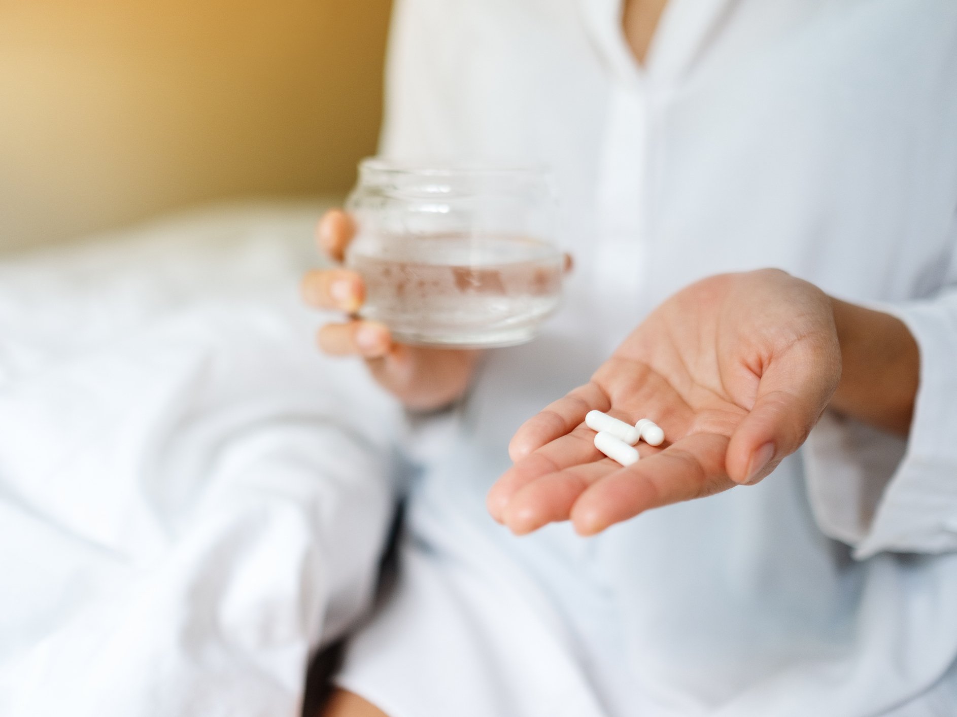 Mano che tiene delle capsule bianche e bicchiere d’acqua, simbolo dell’uso di integratori durante le cure contro il cancro